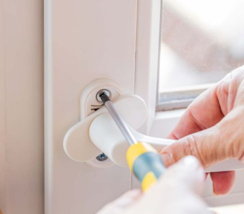 мастер прикручивает оконную ручку к раме окна